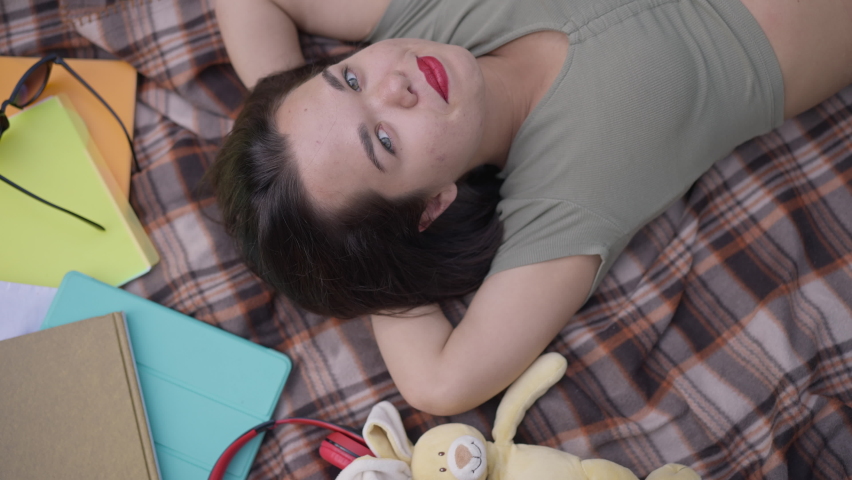 Top view portrait of happy Caucasian little woman looking at camera smiling lying on blanket outdoors. Relaxed carefree person with dwarfism enjoying leisure in spring summer park posing