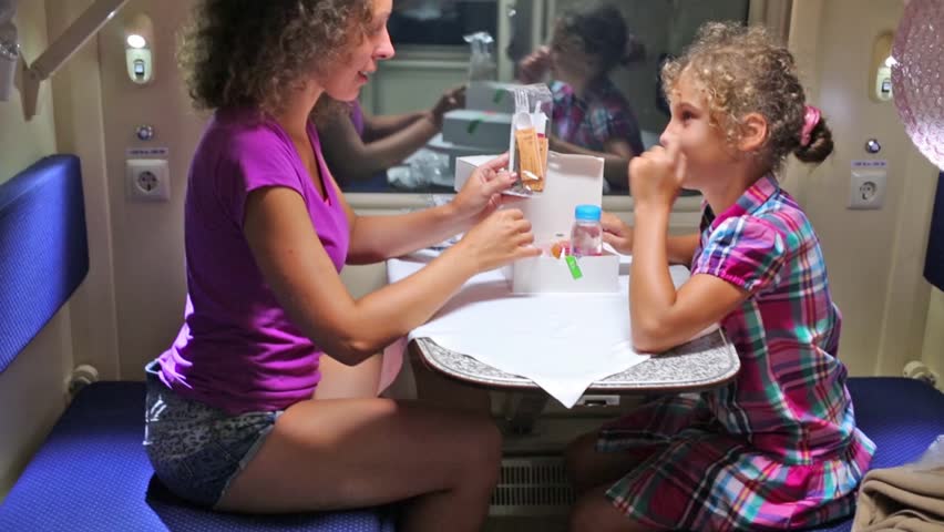 Mother and daughter sit near window of moving train and looks at box with meal