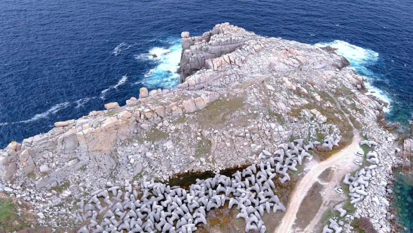 Aerial backward moving shot of paper cliffs along hilly terrain surrounded by sea water in the area of Morás, Xove, Lugo, Galicia, Spain. Gravel pathway.
