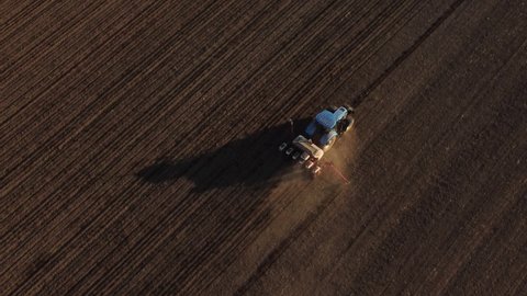 Aerial view of tractor at work in spring field. Time of sowing. Shooting from drone flying over tractor in field with prepared soil for planting, new harvest. Agriculture concept. Rural landscape.