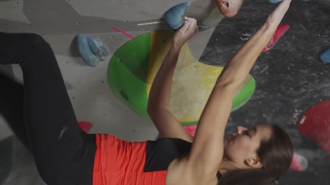 Female professional climber training on a climbing wall, young woman practicing rock-climbing and moving up, vertical video, wellness.