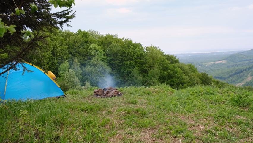 Back view of happy young woman in hat enjoying summer day in nature. Hipster girl holding big American flag in front campsite tent on background beautiful mountains. Independence and July 4th concept