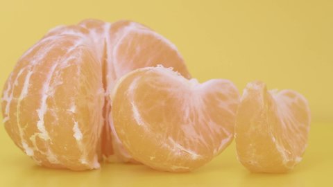 Tangerine slices and whole on the table on a yellow background, water drop falling on the fruit. Slow motion, 8K downscale, filmed on high speed cinema camera. 4K.