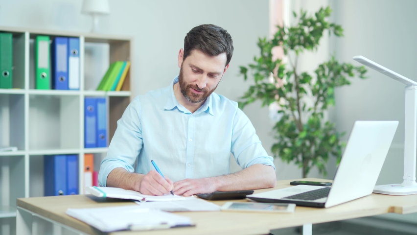 Happy employee, accountant working in the workplace in office counting profit taxes paperwork routine Concentrated young male entrepreneur manager analyzing statistics in paper report, doing financial Royalty-Free Stock Footage #1090601129