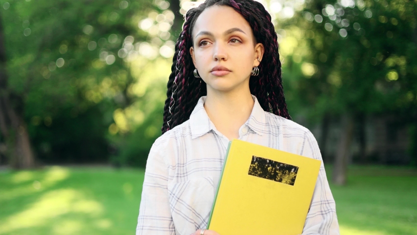 Student girl with dreadlocks standing with books near the university building and looking at the camera. Portrait of attractive girl. 