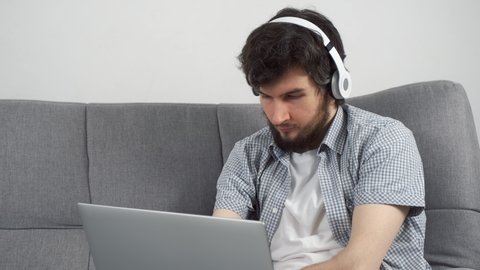 Disabled man with amputated two stump hands in headphones is listening music on laptop at home sitting on sofa. Problem of adaptation to life people with disabilities. Independent Invalid person.