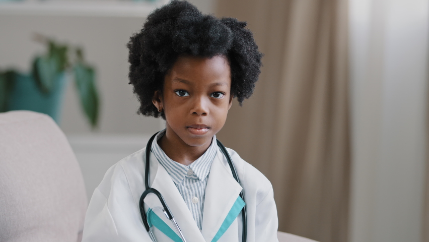 Close-up little cute pretty kid girl in medical clothes pretending to be doctor plays looking at camera posing raises index finger comes up with idea remembers creates plan future profession concept Royalty-Free Stock Footage #1090609545