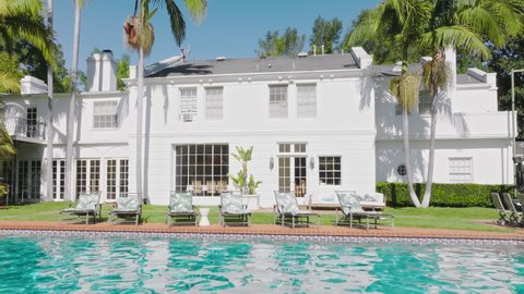 Large white classic architecture house with pool, sun deck and scenic garden with green palm trees on sunny summer day. Cinematic mansion, summer vacation in real estate. Beverly hills USA, Apr 2022 Redaktionel stock-video