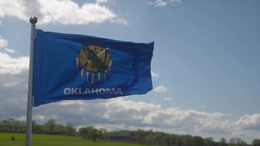Oklahoma flag on a flagpole waving in the wind, blue sky background