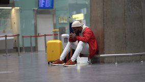 Sad African American man upset at airport his flight is delayed. Depressed traveler male waiting for a plane sitting in empty terminal with baggage. Exhausted guy on a long night connection at airport - Powered by Shutterstock - Get 15% off with code: PIKWIZARD15