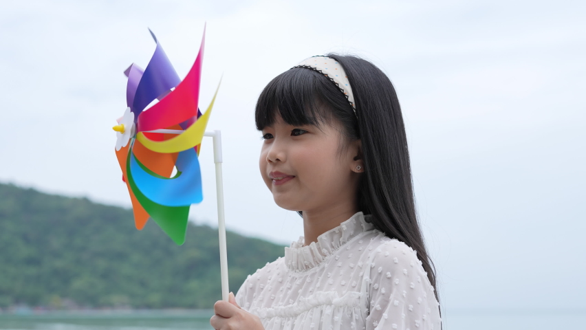 Holiday concept of 4k Resolution. Asian girl smiling happily on the beach. children playing with windmills. summer vacation travel.