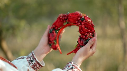 Ukrainian woman holding in hands wreath from red flowers and viburnum. She admires her traditional head decoration