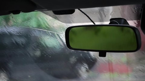 View of the rear-view mirror in the car, in the reflection of which leaves in the rain. 