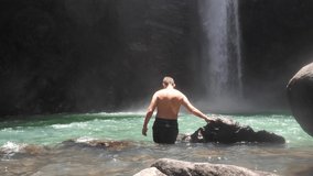 A young Caucasian man bathing in the waterfall cold spring on a hot summer day.