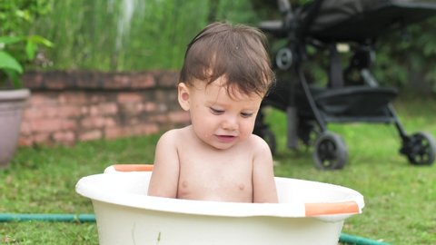 The child is given a plucked flower and he lowers it into the basin. A child in a basin enjoys bathing. The child is given a plucked flower and he lowers it into the basin The baby is 9-10 months old
