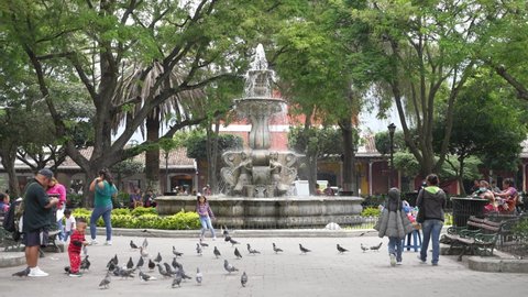 Antigua Guatemala, Guatemala - May 25 2022: Adults and children walking and playing near the fountain at Plaza Central Park.