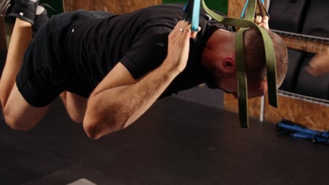 Man doing trx suspension straps. Young man doing push-ups in air while hanging on trx. Fit pretty male doing fly yoga stretching exercises with fitness straps in training. Trainer monitors exercise.