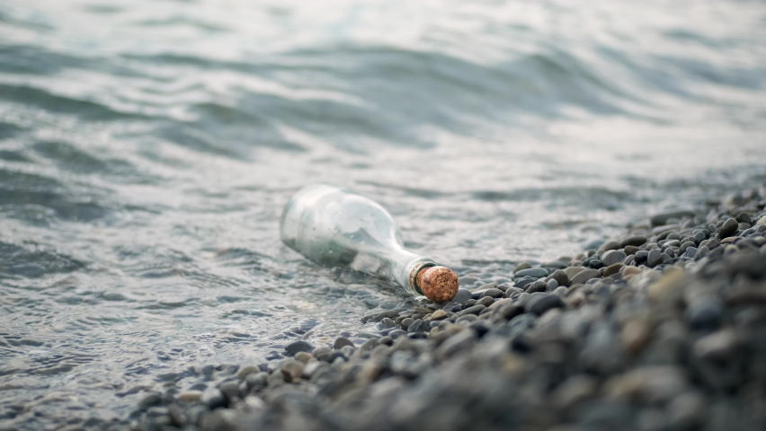 Close up rack focus glass bottle with wooden cork on sea or ocean. concept of note for posterity thrown into water. vintage glass bottle lies on stone beach.