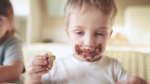 children eat chocolate. dirty little baby kids in the kitchen eating chocolate in the morning. happy lifestyle family eating sweets kid dream concept. baby dirty face eating chocolate cocoa