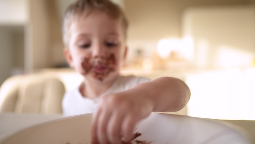 baby boy eat chocolate. dirty little baby kids in the kitchen eating chocolate in the morning. happy family eating sweets kid lifestyle dream concept. baby dirty face eating chocolate cocoa