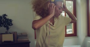 Young Stylish Brazilian Woman With Headphones on and Dancing to the Beat of a Song in her Apartment. Beautiful Carefree Female with Curly Hair Enjoying her Time By Moving Along Happy Music