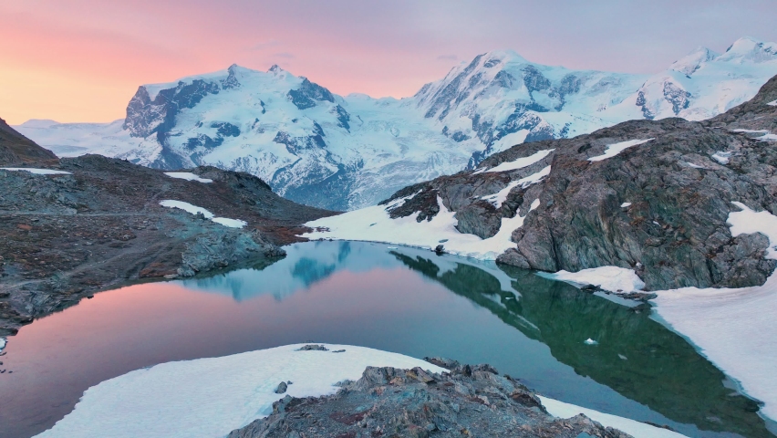 Swiss Alps at dawn, flying over a mountain lake in Switzerland near Gornergletcher and Monte Rosa, beautiful Swiss nature, alpine adventure, snow covered mountain range at sunrise.  Royalty-Free Stock Footage #1090633839
