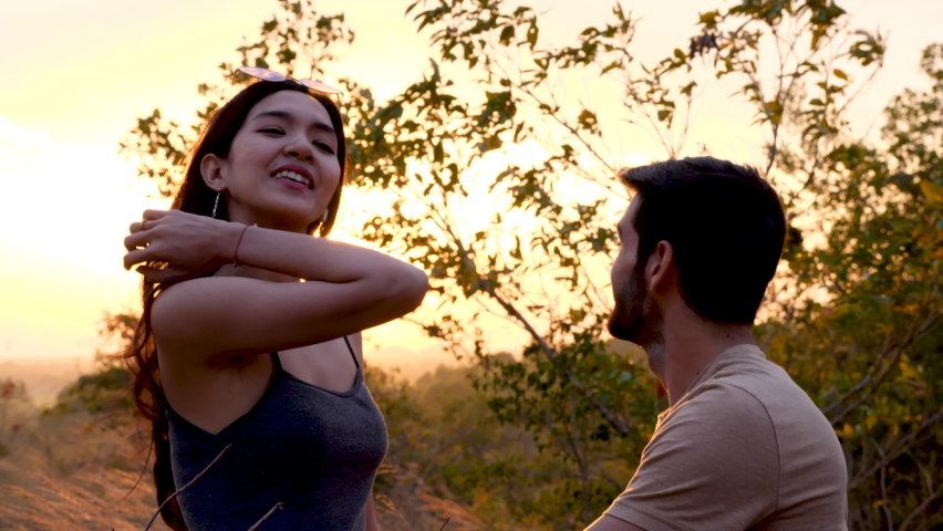 Happy love couple take photo and selfie during camping and relax in forest hiking trip, beautiful Asian woman and caucasian man happiness spend time tpgether, sunset liesure romantic moment