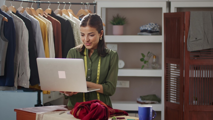 A young modern smling Indian Asian woman or female busy professional fashion designer is working on creative costume designs using a laptop. self-employment woman, empowerment, gender equality concept