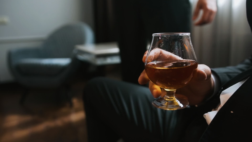 Elegant rich male businessman sitting and resting. The male holds a glass  with a golden drink and raises it to his lips. Gourmet alcoholic beverage. Side view