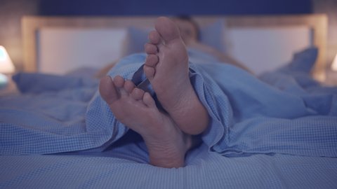 Man lies in bed in the evening with his legs crossed in pads, moving his feet, close-up of his feet