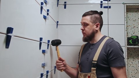 Tiler knocks the wedges of the ceramic tile leveling system off the wall in the bathroom, Slow motion