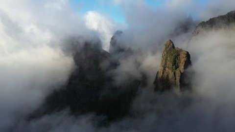 Drone shot moving sideways among the foggy peaks of Pico das Torres in Madeira.