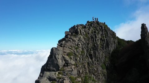 Drone shot moving backwards away from a group of 3 friends standing on the peak of Pico das Torres in Madeira.