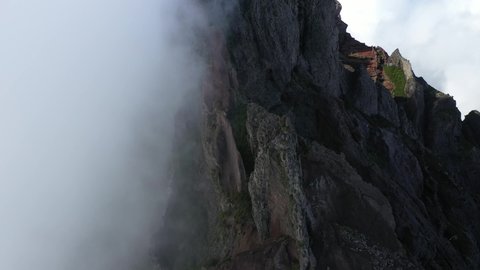 Drone shot moving slowly up over the foggy peak of Pico das Torres in Madeira.