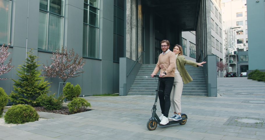 Happy young caucasian couple smiling and enjoying riding of electric scooter together in city near modern office centre. Outside, lifestyle concept Royalty-Free Stock Footage #1090651331