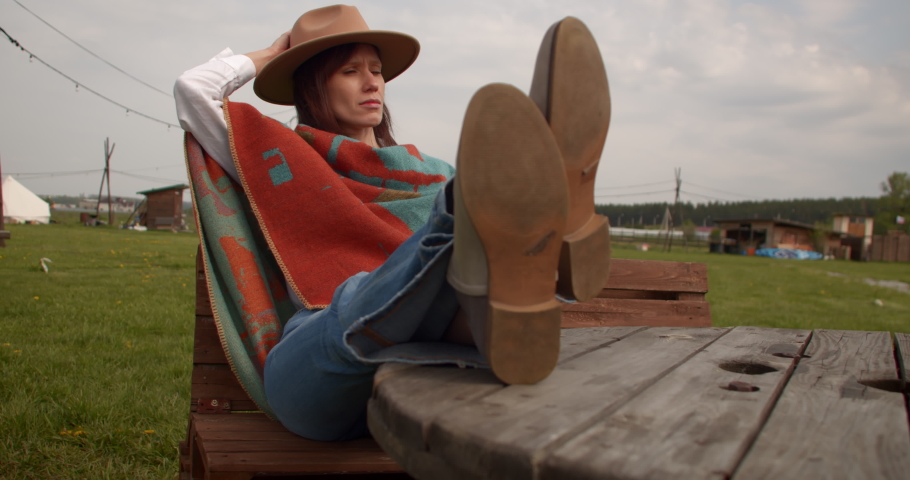 Stylish american countryside woman in a hat and poncho sit on back yard of his country house