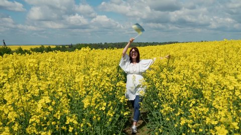 Ukraine, the Lviv region, the young pregnant girl cheerfully runs among rapeseed in a rapeseed field with a flag of Ukraine