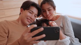Happy asian family with daughter using phone together in the living room at home. Parents and child girl watching social media funny videos, Searching online on smartphone looking for humor program.