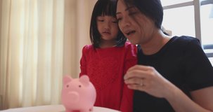 4K Video slow motion asian girl and mom put coin into piggy bank. Concept for financial and saving bank for family.