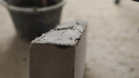 Bricklayer applies adhesive glue on autoclaved aerated concrete blocks with notched trowel and spatula. Brickwork worker contractor puts mortar on foam concrete doing masonry on construction site.