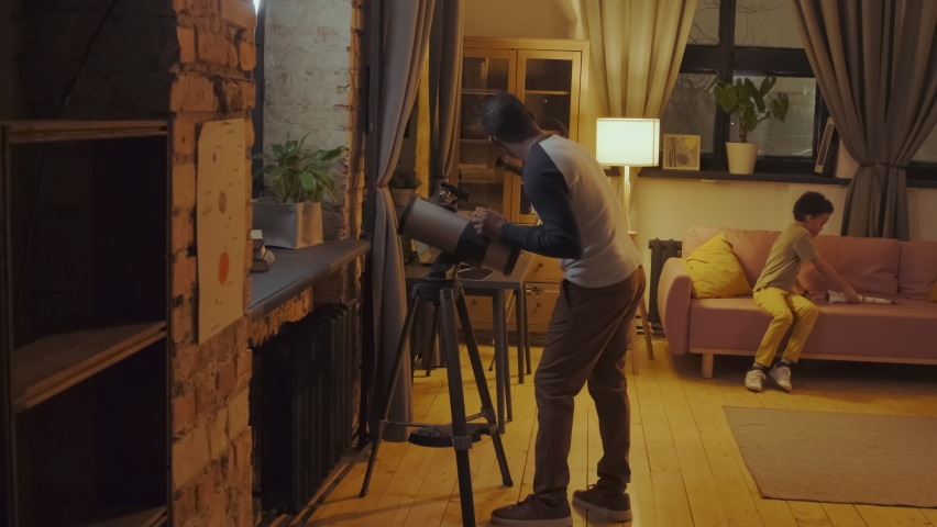 Young African American boy joining his father to watch stars and planets using telescope at home