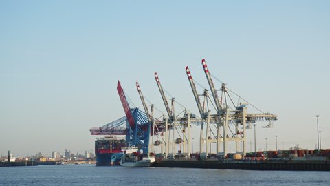 HAMBURG, GERMANY - MARCH 19, 2022: Container Terminal with Ships being loaded in the busy Port of Hamburg in sun. Large Container Cranes.