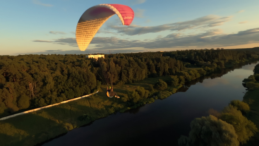 Dynamic aerial shot of paraglider flying along the river and against sunset Royalty-Free Stock Footage #1090668863