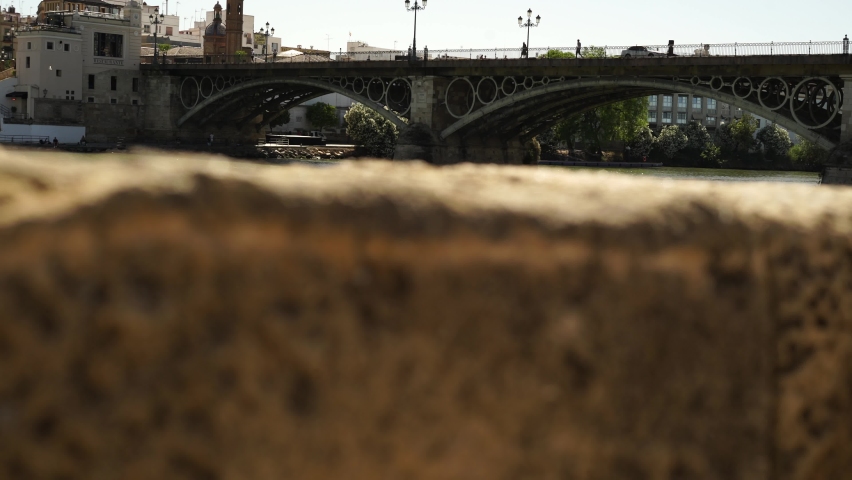 Wall and the Triana bridge in the background with the Guadalquivir river and people walking over the bridge. Seville famous landmarks. Andalusia, Spain. Seville. Tourism.