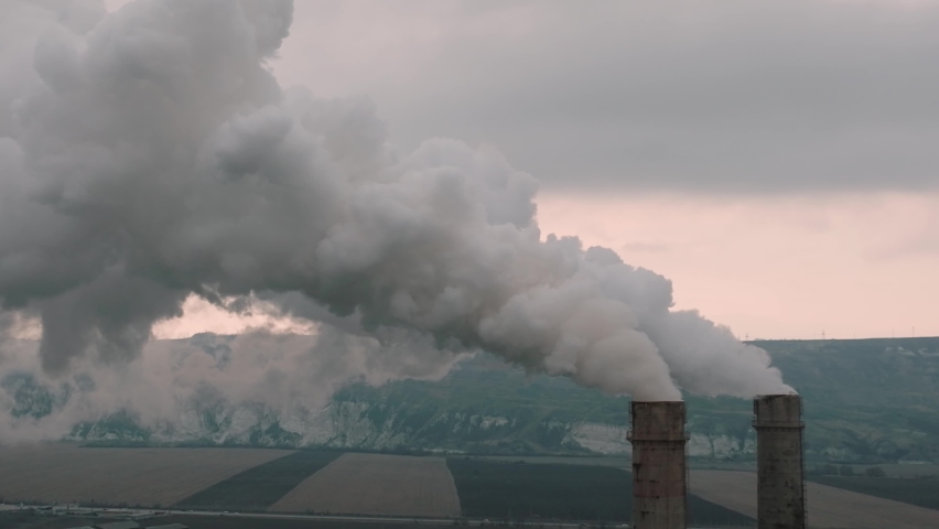 Air pollution from smoke coming out of two factory chimneys. Industrial area in the city aerial view. Global warming