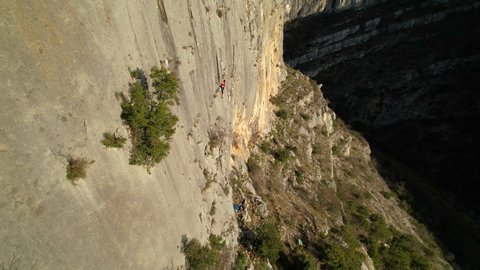 AERIAL: Flying close to sunlit climbing wall and approaching female rock climber. Adrenaline outdoor activity in beautiful and picturesque environment. Sporty young woman lead climbing the rock wall.