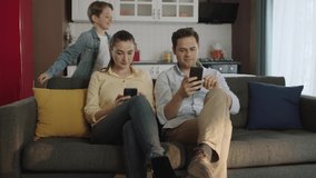 Happy family smiling at camera.Young parents looking at their social media accounts on their smartphones with their young son hugging them from behind.