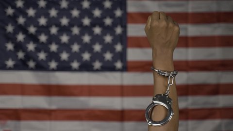 Close up shot of hanads rising with released cuffs against us or american flag as background - concept of juneteenth, freedom and justice.