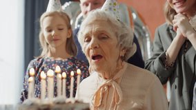Joyous family in party hats hugging elderly grandmother after she blowing candles on birthday cake during home celebration - Powered by Shutterstock - Get 15% off with code: PIKWIZARD15