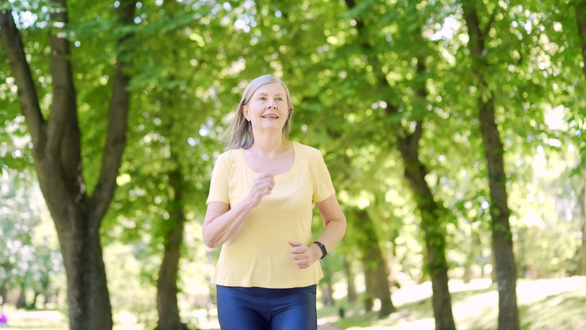 Senior active gray-haired woman morning jogging in the urban city summer park outdoor. Mature old fitness female running exercise. Healthy Lifestyle. Elderly sport runner woman training Workout cardio